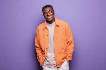 Obraz premium Portrait of a smiling young African man with hands in pockets set against a purple background