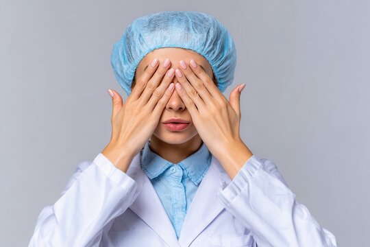 Young white female doctor in scrubs covering her eyes and signaling to stop showing sadness and fear Embarrassment and negativity