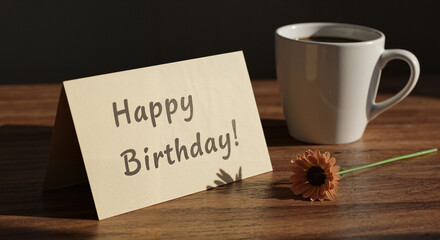Birthday card with message next to coffee cup and flower on wood  