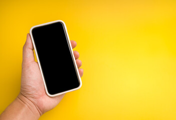 Hand holding smartphone with blank black screen on yellow background, perfect for app design, UI mockup, mobile technology, social media, online marketing, communication, and digital business concept.