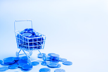Online shopping, sales profit, e-commerce growth, fintech, inflation, digital financial, e-wallet, money technology concept. Full of coins in mini white shopping cart on white background, blue tone.