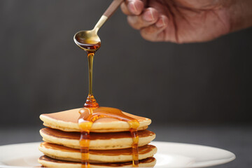 A hand pours golden maple syrup onto a stack of fluffy pancakes, a delicious breakfast treat