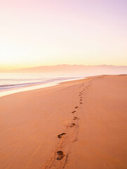 Footprints in the sand on a beach at sunrise with calm ocean waves and a distant horizon