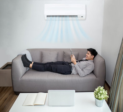 Business man in formal shirt playing tablet computer while lying on safa and relaxing under the air conditioner at home.