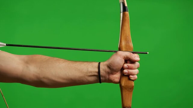 Archer Pulling Bowstring, Green Screen - Close-up of a male archer's arm and hand drawing back the string of a bow, aiming an arrow. The shot is against a bright green screen, ideal for compositing.