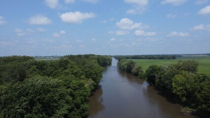 Fototapeta premium Serene river flowing through lush green forests under a partly cloudy sky