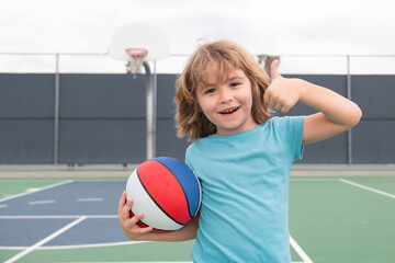 Child playing basketball on outdoor court. Happy child boy hold basketball ball. Summer sport kids. Kid on basketball game. Sporty kid training basketball on playground. Outdoor activity for children. © Volodymyr
