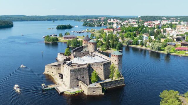 Drone flying around the Olavinlinna castle while boats move past it, in Finland