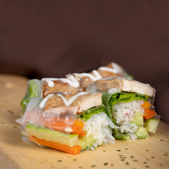 Fresh spring rolls with tofu, lettuce, carrots, cucumber, and rice noodles, arranged on a wooden board, drizzled with creamy sauce.