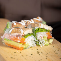 Fresh spring rolls with tofu, lettuce, carrots, cucumber, and rice noodles, arranged on a wooden board, drizzled with creamy sauce.