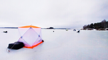 Bright orange ice fishing shelter set against a gray winter landscape on a frozen lake in early morning light