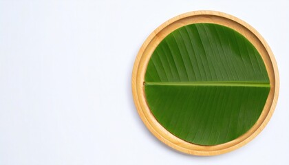 Fresh green banana leaf on a round wooden plate, flat lay on white background with copy space