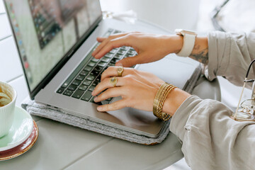 Obraz premium Close-up of a woman working on laptop at outdoor cafe, hands typing on keyboard with coffee cup on table, remote freelance work concept