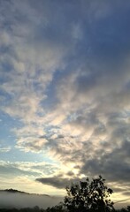 summer morning, dawn, dark clouds in the blue sky, fog rising over the forest
