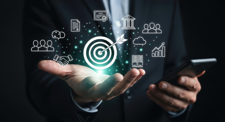 Strategic Business Goals and Objectives Concept with Hand Holding Smartphone Displaying Target Icon and Related Symbols Representing Achievement and Success in Digital Era