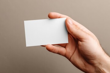 Fototapeta premium Hand holds a blank card on a neutral background for mockup purposes, ideal for design projects and presentations showcasing branding concepts or personal information