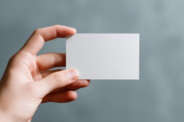 Fototapeta premium Hand is holding a blank card suitable for designing custom templates or mockups in a minimalistic style against a soft gray background