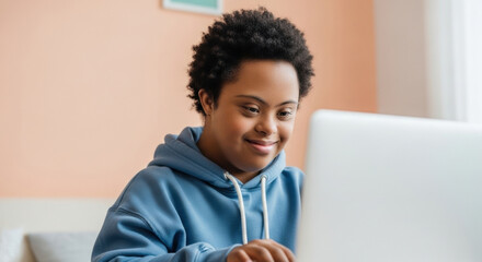 Smiling young woman with down syndrome wearing blue hoodie using laptop at home, engaging in online learning or remote work, fostering inclusion and independence