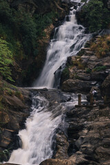 Obraz premium Kuda Ravana Waterfall cascading down rocky terrain in Sri Lanka with tourist admiring the scenery and taking pictures from a wooden platform