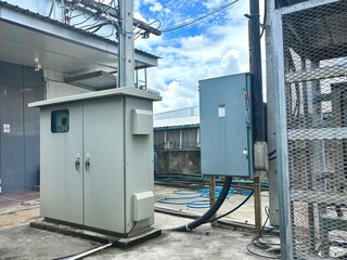 An outdoor electrical control cabinet and industrial equipment, representing the complex infrastructure and power management systems of a factory or commercial building under a bright sky.
