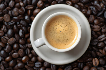 Fototapeta premium A top-down perspective of a tiny white espresso cup with frothy cream, resting on a saucer amidst a background of dark roasted coffee beans.