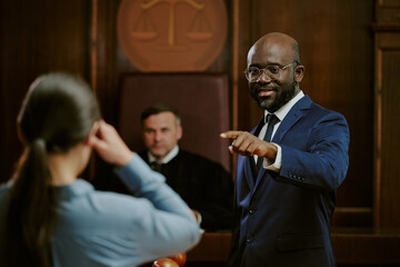 Black middle aged man in suit standing and gesturing while addressing Caucasian woman in courtroom...