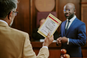 Middle aged Caucasian man holding evidence bag while standing in courtroom, Black man in suit...