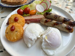 Two poached eggs served with hash brown, pork sausages and bacon