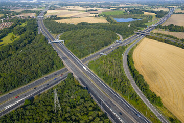 Aerial view of Croft Interchange (Junction 21A) near Birchwood, where the M6 and M62 motorways meet, surrounded by woodland, golden farmland, and a small lake under a clear summer sky. © bardhok