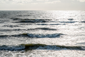 Gentle waves roll across the surface of a sunlit sea, creating a rhythmic pattern.