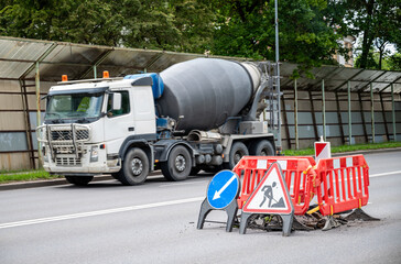Concrete mixer truck on a road, near a worksite marked by red barricades and caution signs...