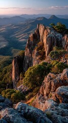 Rocky mountain peak at sunset. Lush vegetation clings to jagged cliffs.  Vast vista of distant hills