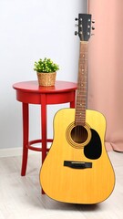 Acoustic guitar leans against a small red side table, a potted plant sits atop
