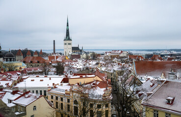 Naklejka premium Winter panoramic view of snowy rooftops and St Olaf church in Tallinn old town