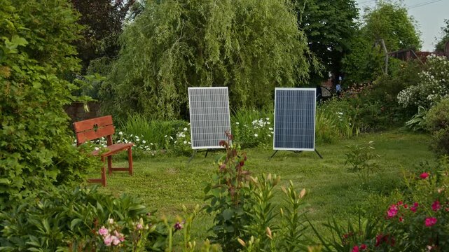 Background shot of two large solar panels on green lawn in picturesque flower garden powering country house handheld style, copy space