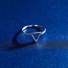 A minimalist silver ring with a small triangle resting on a deep, sparkling, textured blue surface.