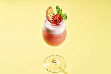 A refreshing cocktail with a flower garnish, served in a stemmed glass on a bright green background.