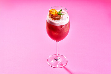 A refreshing cocktail with a flower garnish, served in a stemmed glass on a bright green background.