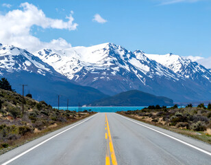 Fototapeta premium Scenic road leading to snow-capped mountains and a turquoise lake under a blue sky, conveying travel, adventure, and vast natural beauty.