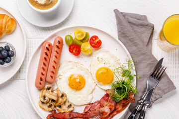 A classic breakfast plate featuring sunny-side-up eggs, crispy bacon, sausages, and fresh tomatoes