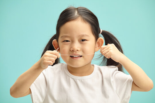 Lovely five years old chinese girl cleans herself teeth by means dental floss, headshot portrait on blue isolated. 