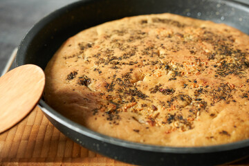 Freshly baked pie with spices in a frying pan on a wooden board