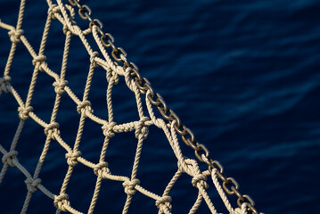 Fototapeta premium Close-up of a nautical net made of rope with a chain link, set against a blue ocean background