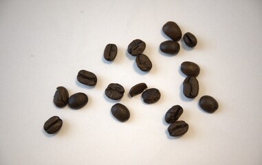 Close-up of roasted coffee beans scattered on a white background. Ideal for food or beverage concepts.