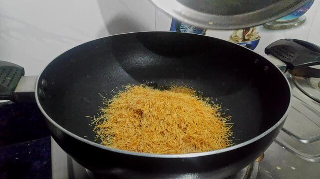 A closeup shot of frying dry semiya or vermicelli or seviyan in nonstick deep fry pan in house