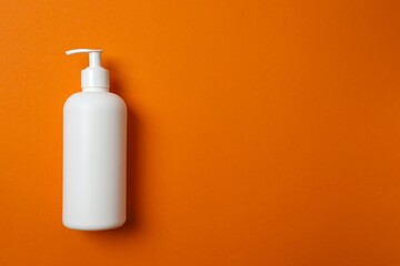 Skincare white bottle on orange background, top view