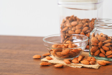 Almonds in glass bowl on wooden table background. Almonds in glass jar.