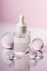 Mockup of glass dropper bottle with face serum or essential oil on pink background with glass balls. The concept of beauty cosmetics, natural products for moisturizing and restoring the skin.