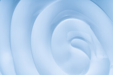 Close-up of a creamy cosmetic gel texture featuring smooth, flowing circles. The soft blue color and minimalist aesthetic create a soothing, elegant visual.