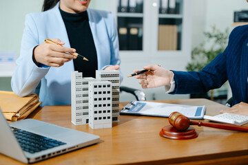 Two professional women reviewing a real estate contract with gavel, building model, and paperwork....